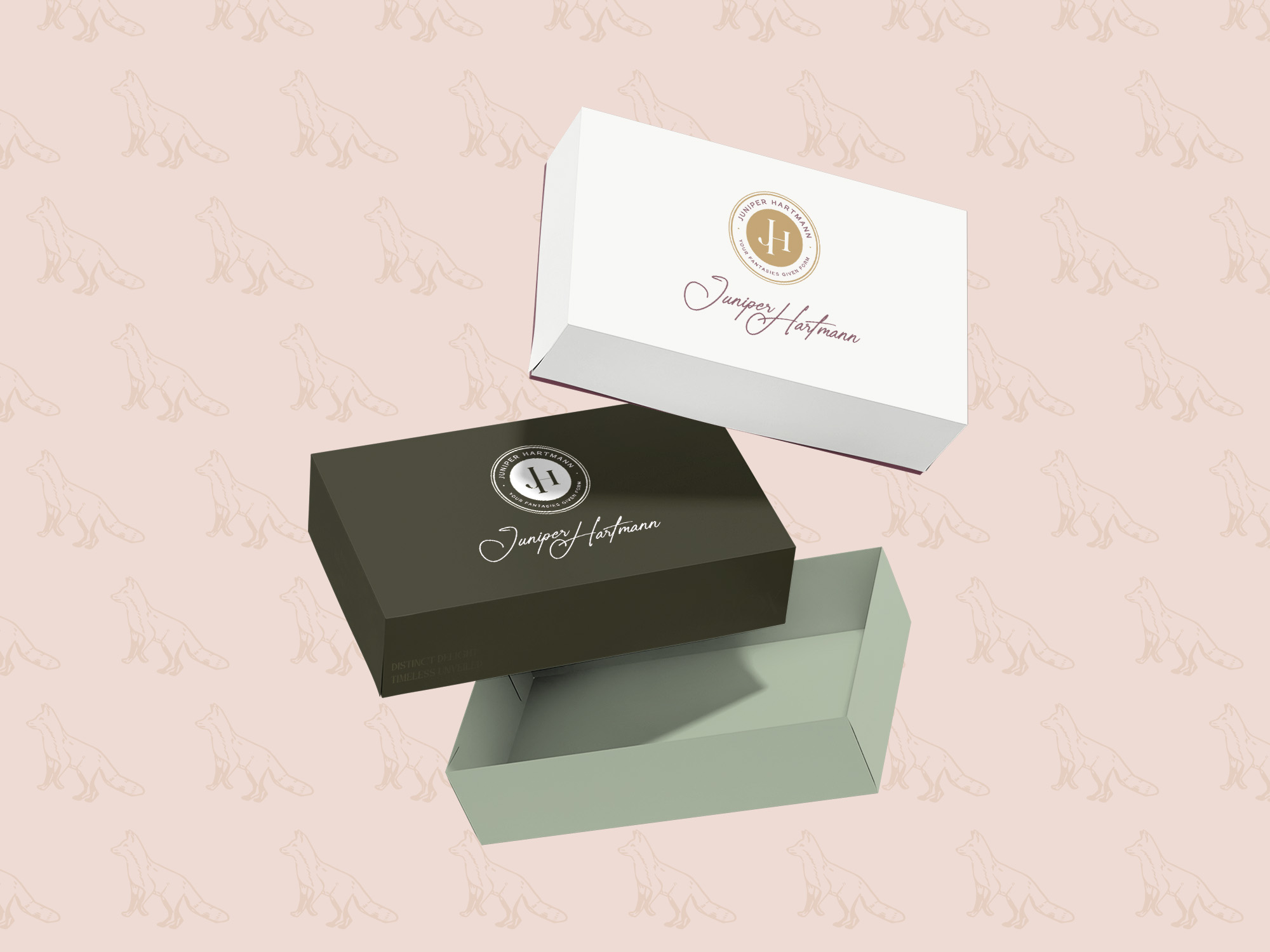 A set of luxury-style packaging boxes designed for the Juniper Hartmann brand. The boxes are in white and deep green with elegant gold accents, featuring the Juniper Hartmann logo in a circular emblem. The background is a soft beige with a subtle fox illustration pattern.